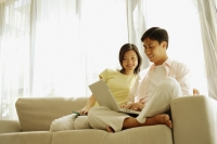 Young couple sitting on sofa side by side, using laptop - Alex Microstock02