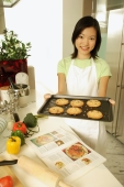 Young woman holding out baking tray, looking at camera - Alex Microstock02