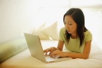 Young woman lying on bed, using laptop - Alex Microstock02