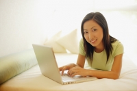Young woman lying on bed, using laptop, looking at camera - Alex Microstock02