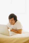 Young man lying on bed, using laptop - Alex Microstock02