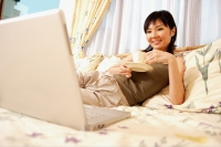  Young woman on bed with cup and saucer, looking at laptop - Alex Microstock02