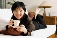Woman lying on sofa, holding cup and saucer - Alex Microstock02