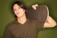  Young man holding skateboard over shoulder, looking at camera - Alex Microstock02