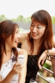  Young women looking at each other, one holding mobile phone - Alex Microstock02