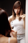 Young woman looking at mirror, touching her hair, frowning - Alex Microstock02