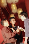 Young men in night club holding out drinks, laughing - Alex Microstock02
