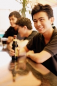 Young man at bar counter with beer bottle, people in the background - Alex Microstock02