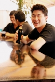 Young man at bar counter with beer bottle, smiling at camera - Alex Microstock02