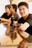 Young man at bar counter holding beer bottle, people in the background - Alex Microstock02