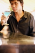 Young man at bar counter holding and looking at cocktail glass - Alex Microstock02