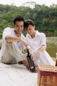 Couple sitting by a lake, with picnic basket, opening bottle of wine - Alex Microstock02