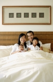 Father and mother with two children in bed, portrait - Jade Lee