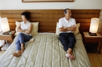 Older couple lying apart on bed, arms crossed - Jade Lee