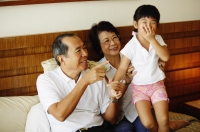 Grandparents with granddaughter, granddaughter covering mouth with hand - Jade Lee