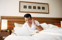 Man on bed using laptop and mobile phone - Jade Lee