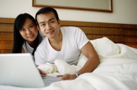 Couple in bed with laptop, looking at camera - Jade Lee