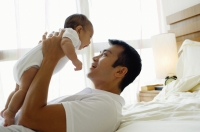 Father carrying baby daughter, lying on bed - Jade Lee