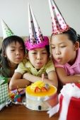 Three girls with party hats blowing candle on birthday cake - Jade Lee
