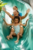 Three girls going down water slide, arms outstretched - Jade Lee