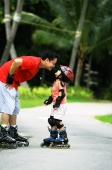 Father and daughter wearing inline skates, father bending to kiss daughter - Jade Lee
