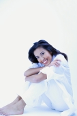 Woman in white shirt and pants, hugging knees, smiling at camera - Alex Microstock02