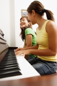 Mother and daughter sitting side by side in front of piano, mother smiling - Alex Microstock02