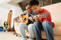 Father teaching son to play guitar, mother and daughter in the background - Alex Microstock02