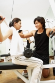 Couple working out in gym, woman lifting weights, man helping her - Alex Microstock02