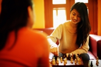 Two young women sitting, playing chess, over the shoulder view - Alex Microstock02