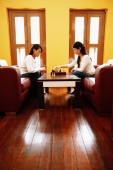 Young women sitting in living room, playing chess - Alex Microstock02