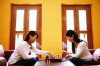 Young women sitting in living room opposite each other, playing chess - Alex Microstock02