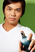 Young man holding bottle of perfume, pointing spray at camera - Alex Microstock02