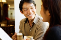 Couple sitting, holding coffee cups, smiling at each other - Alex Microstock02