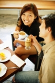 Couple at cafe, holding cups of coffee, woman looking up at camera - Alex Microstock02