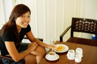 Young woman sitting, food and coffee in front of her, looking at camera - Alex Microstock02