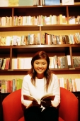 Young woman, sitting on chair, reading book, bookshelf behind her - Alex Microstock02
