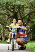 Girl on bicycle, father crouching down next to her, both looking at camera - Alex Microstock02