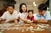Family in living room, sitting side by side, working on jigsaw puzzle - Alex Microstock02