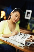 Young woman sitting at table, reading newspaper - Alex Microstock02