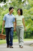Couple holding hands and walking in park, man carrying picnic basket - Alex Microstock02