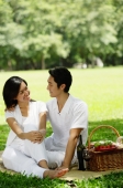Couple sitting with picnic basket, smiling at each other - Alex Microstock02