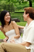 Couple sitting face to face on park bench, woman laughing - Alex Microstock02
