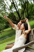Couple sitting on park bench, looking up, man pointing - Alex Microstock02