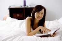 Young woman lying on bed, holding book, looking at camera - Alex Microstock02