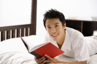 Man lying on bed, reading book, smiling at camera - Alex Microstock02