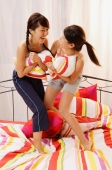 Two young women having pillow fight on bed - Alex Microstock02