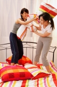 Two young women having pillow fight on bed - Alex Microstock02