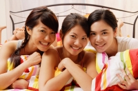 Three young women lying side by side on bed, smiling at camera - Alex Microstock02