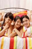 Three young women lying side by side on bed, looking at camera, smiling - Alex Microstock02